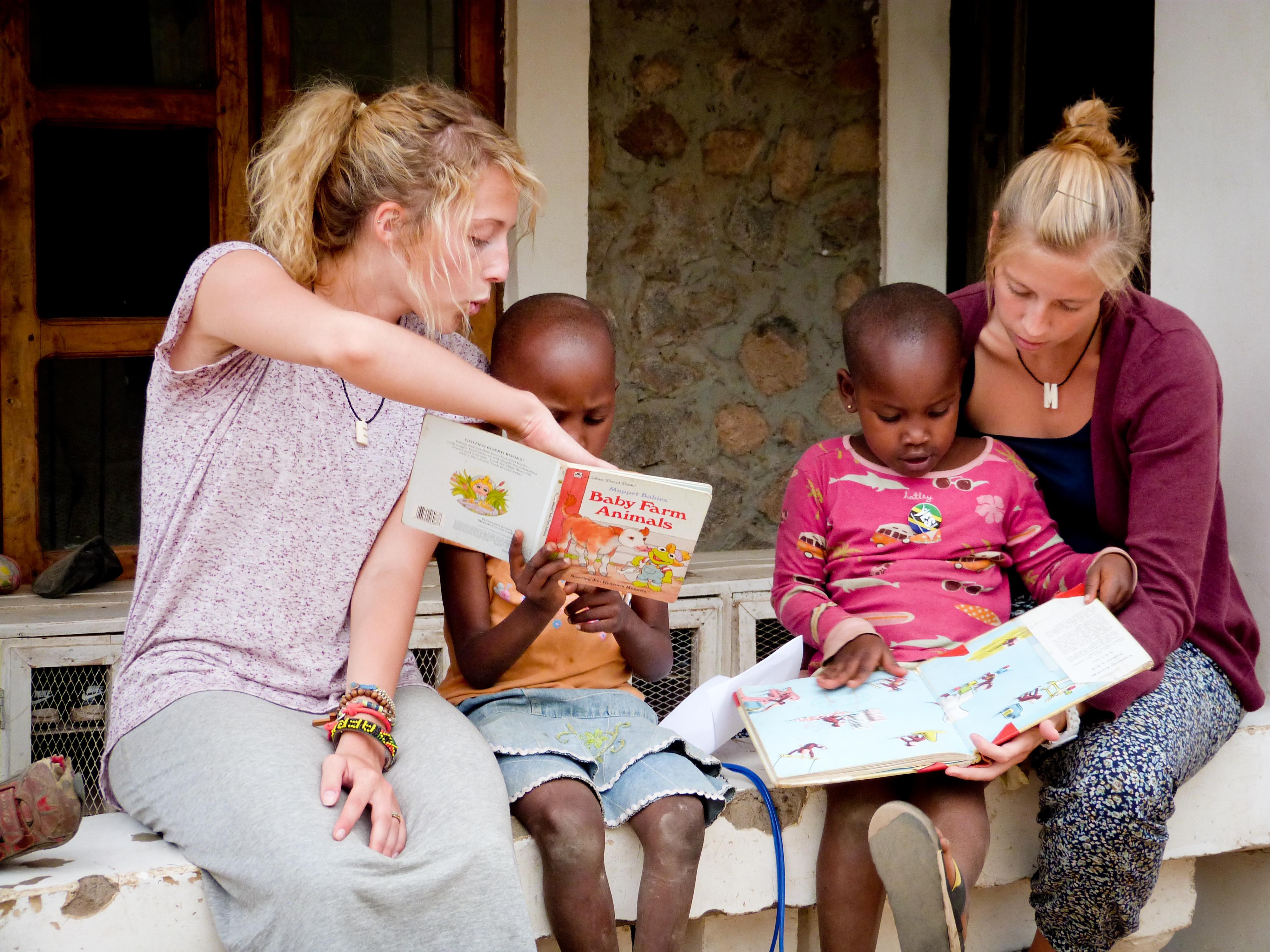Voluntarias de enseñanza ayudan a niñas a leer en inglés. Voluntarias leen a un par de niñas como parte de su voluntariado para enseñar inglés en Tanzania.